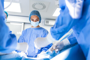 Wall Mural - Surgeons operating below lighting equipment. Male and female doctors are wearing blue scrubs. They are working in hospital.