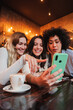 © Jose Calsina - Vertical portrait of a group of young women having fun sharing media with an cellphone. Females looking the smartphone on a coffee shop. Girls shopping online on a marketplace using a mobile phone