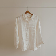 Wall Mural - White crumpled shirt, blouse on hanger over white wall. Aesthetic female fashion clothes, wardrobe concept