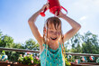 © Westend61 - Smiling girl pouring water on head from red watering can in balcony