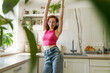 © Westend61 - Happy young woman with arms raised dancing in kitchen at home