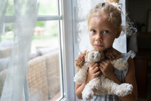 Sad Girl Holding Stuffed Toy Standing Near Window At Home