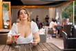 Beautiful cute woman drinking cocktail while waiting for meeting with friends at restaurant terrasse in metropolis on summer. Beautiful female enjoy outdoor lifestyle in the city