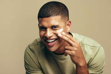 Happy young man using a beauty cream on his face to keep it healthy and fresh