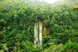 Majestic waterfall cascading over lush green hills in a tropical environment, framed by lush trees.