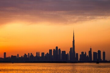 Wall Mural - Silhouette view of Dubai city skyline against the orange dusk sky as seen from the sea at sunset