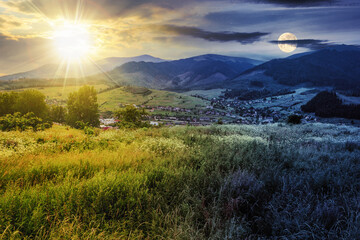 Wall Mural - day and night time change concept. meadow with wild herbs on a hillside facing the settlement in mou
