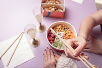 Attractive couple of casual caucasian girls eating delicious poke, japanese fresh healty food, during lunch. Young white pretty women relaxing talking eating tasty sushi sitting at table on a date