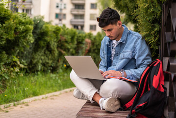 A male college student using a laptop outside.