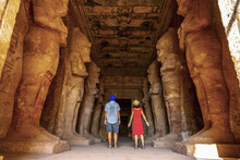 A Tourist Couple At The Abu Simbel Temple Next To The Sculptures, In Southern Egypt In Nubia Next To Lake Nasser. Temple Of Pharaoh Ramses II, Travel Lifestyle