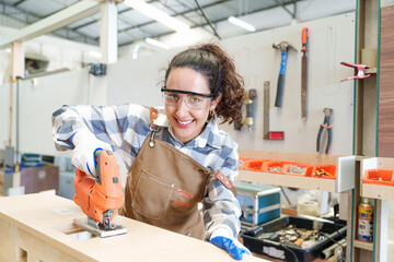 Young Caucasian carpenter working with drill on the desk workshop for the production of furniture, warehouse storage, Production line of the wooden working industrial factory