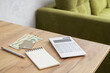 Calculator, money, journal and pan on the desk agaisnt green sofa. oncept of estimate utility costs