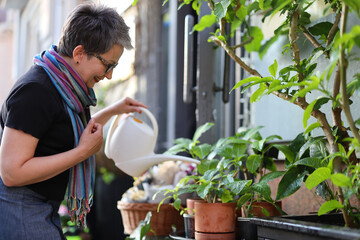 Poster - Positive senior woman watering home plants outside.