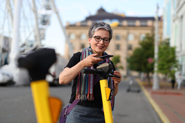 Sticker - Senior woman uses an app in her smartphone to rent an electric scooter.