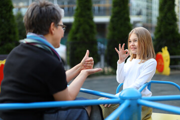 A deaf girl speaks sign language With a teacher on the playground.