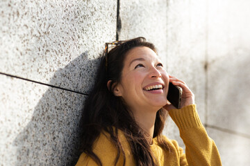 Beautiful young asian woman leaning against wall and talking on phone