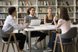 © fizkes - Diverse group of fresh students studying together in university campus, sitting at table in library, talking, discussing education, class project, working on home assignment in multiethnic team