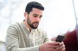 © mimagephotos - Handsome arabic man listening to music with mobile phone sitting outdoors