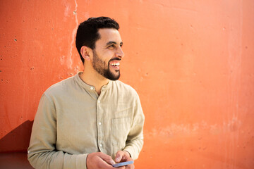 Wall Mural - Cheerful young arabic man with mobile phone against orange wall