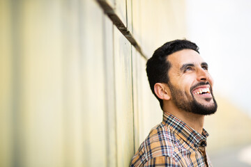 Wall Mural - Handsome young arab man leaning to a wall looking away and smiling