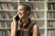 © fizkes - Cheerful pretty young student girl talking on mobile phone, standing in college library with bookshelves in blurred background, speaking on cellphone, laughing, smiling, enjoying telephone call