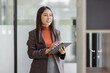 © David - Young business entrepreneur Asian woman wear glasses using tablet , standing near the window in workplace business finance concept.