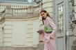 Fashionable elegant confident woman wearing trendy pink suit blazer, wide trousers, with green faux leather shoulder bag, walking in street. Outdoor fashion portrait. Copy, empty space for text
