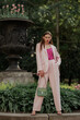 Fashionable elegant woman wearing trendy pink suit with classic blazer, satin top, wide leg trousers, holding green faux leather bag, posing in street. Full-length outdoor fashion portrait
