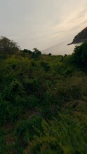 Vertical Video 4k. Aerial View Cinematic Tropical Island Mountain Lush Greenery Rock Seashore Lagoon Sea Water Sunset. FPV Sport Drone Shot Flying Over Cliff Covered Plant Vegetation Sunrise Seascape