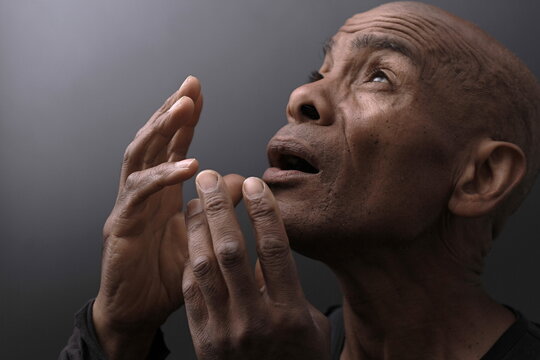 man praying to god with hands together with depression on grey background stock photo	