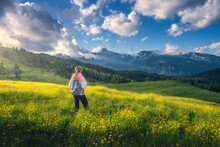 Girl On The Hill With Yellow Flowers And Green Grass In Beautiful Alpine Mountain Valley At Sunset In Summer. Landscape With Young Woman In Alps, Rees, Sky With Clouds. Travel And Hiking. Slovenia