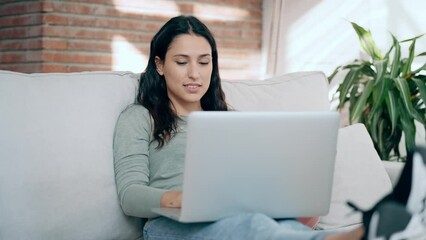 Wall Mural - Video of beautiful young woman working with her laptop while sitting on a couch at home.