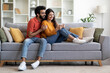 © Prostock-studio - Happy indian man and woman using smartphone while relaxing on couch together