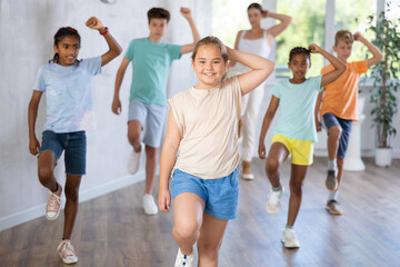 Wall Mural - Portrait of cheerful preteen girl enjoying active dancing during group training in dance studio..