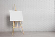 © New Africa - Wooden easel with blank canvas near white brick wall indoors. Space for text