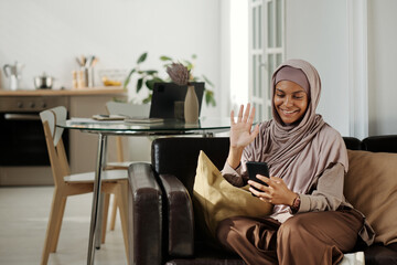 Aufkleber - Happy young Muslim woman waving hand to her friend or husband on smartphone screen while communicating in video chat at home