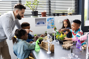 Wall Mural - Diverse elementary schoolchildren and male teacher studying plants together in school class