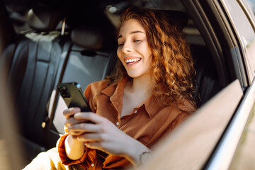 smiling woman using smartphone while sitting in the back seat of a car. young woman checks mail, tex
