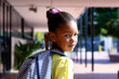 Portrait of happy biracial schoolgirl with school bag, turning to camera outside school, copy space