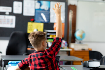 Sticker - Rear view of caucasian schoolboy sitting at desk raising hand in class