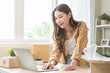 canvas print picture - Online sell store, startup small business entrepreneur asian young woman using laptop computer check order purchase from web, owner working at home office, preparing pack product parcel for delivery.