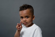 A toddler of African American background poses for a portrait and gives a peace sign.