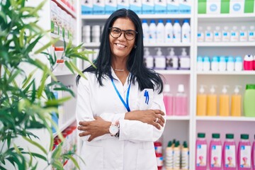 Wall Mural - Middle age hispanic woman pharmacist smiling confident standing with arms crossed gesture at pharmacy