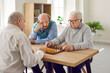 Group of pensive senior people playing chess in elderly care house or retirement home. Three old men sitting at table, looking at chessboard and thinking about game strategy