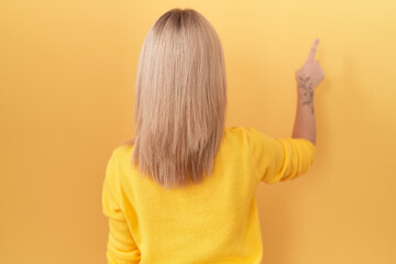 Canvas Print - Young caucasian woman wearing yellow sweater posing backwards pointing ahead with finger hand