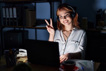 Poster - Young caucasian woman working at the office at night smiling with happy face winking at the camera doing victory sign. number two.