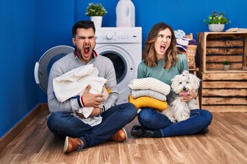 Canvas Print - Young hispanic couple doing laundry sitting on the floor angry and mad screaming frustrated and furious, shouting with anger. rage and aggressive concept.