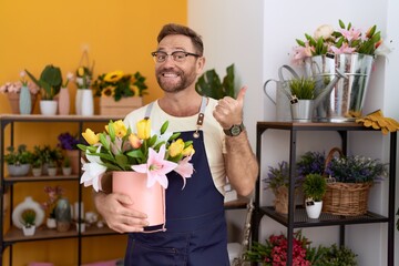 Sticker - Middle age man with beard working at florist shop holding plant smiling happy and positive, thumb up doing excellent and approval sign