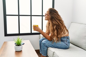 Wall Mural - Young beautiful hispanic woman drinking coffee sitting on sofa at home