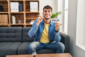 Canvas Print - Young hispanic man at therapy asking for help surprised with an idea or question pointing finger with happy face, number one